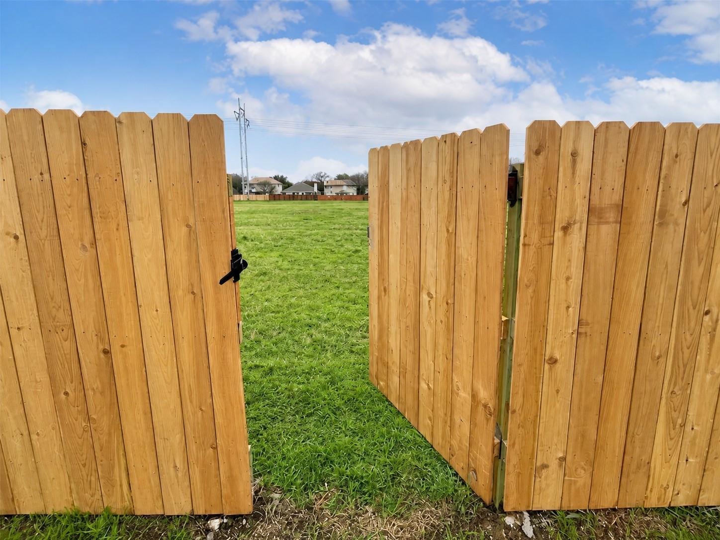 Wood privacy fence with an open gate providing access to a grassy expanse