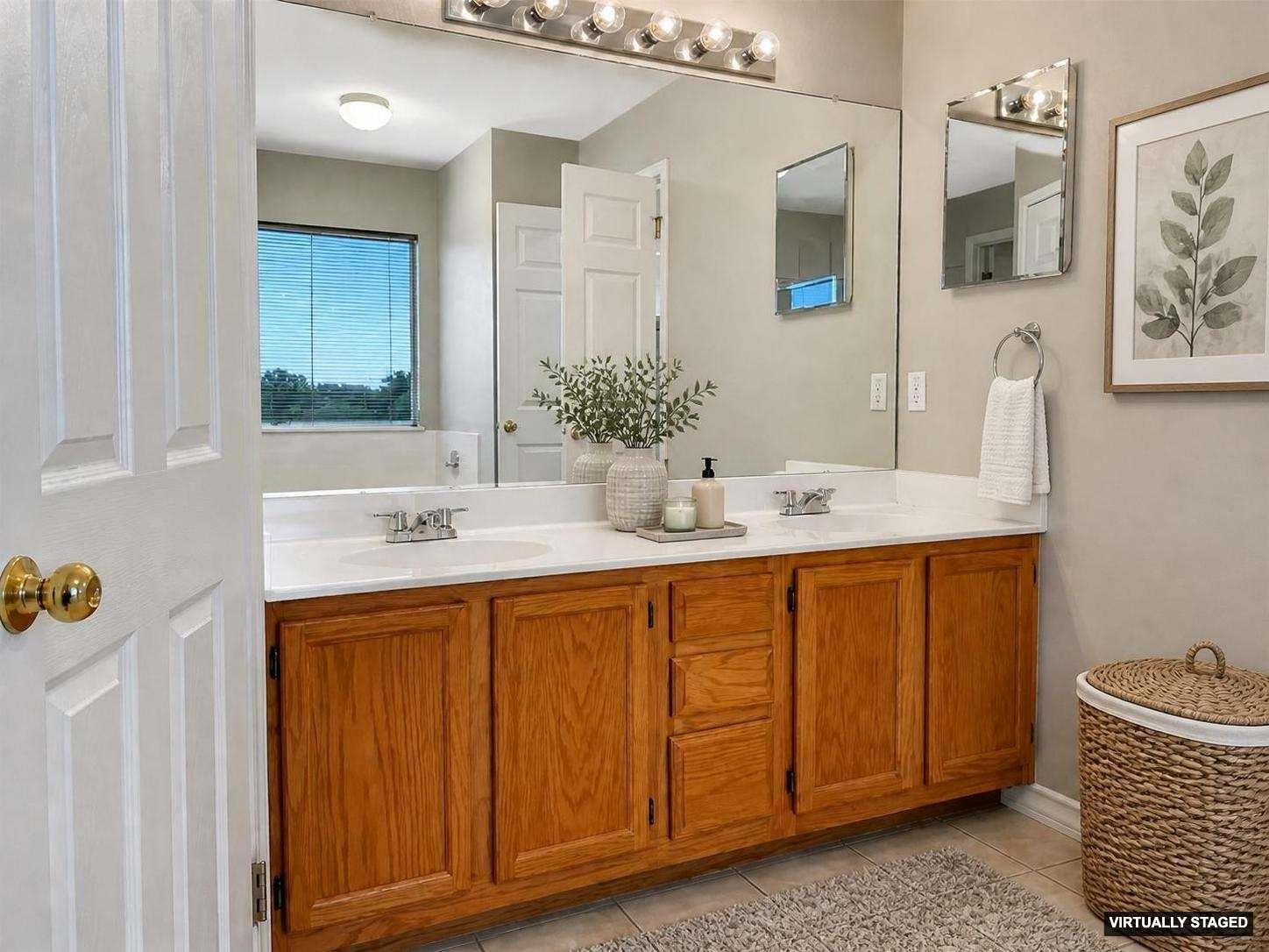 Bathroom featuring a dual-sink vanity with wood-finish cabinetry, a large mirrored wall, and overhead vanity lighting