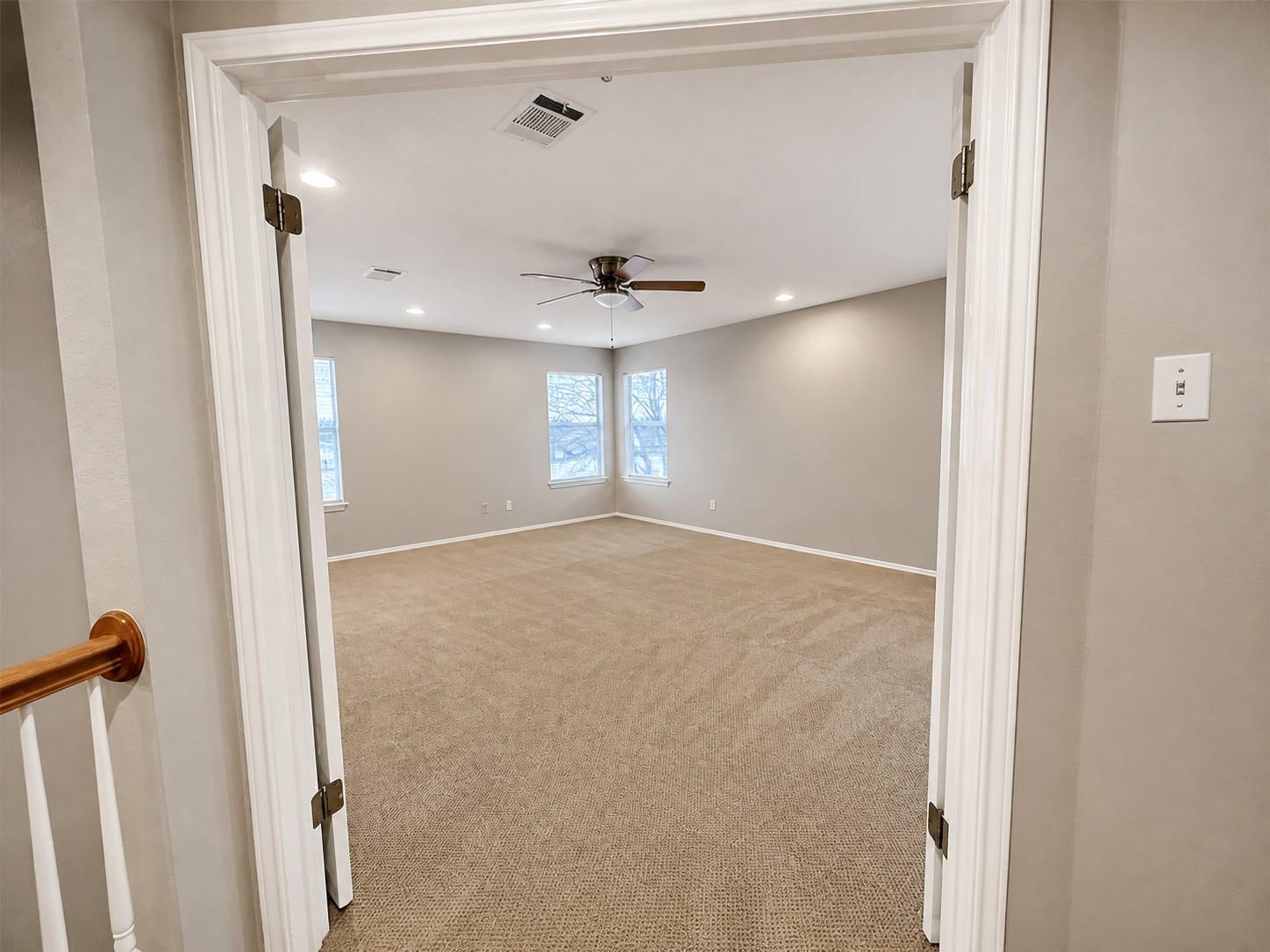 Spacious room featuring neutral carpet flooring, light gray walls, multiple windows, recessed lighting, and a ceiling fan