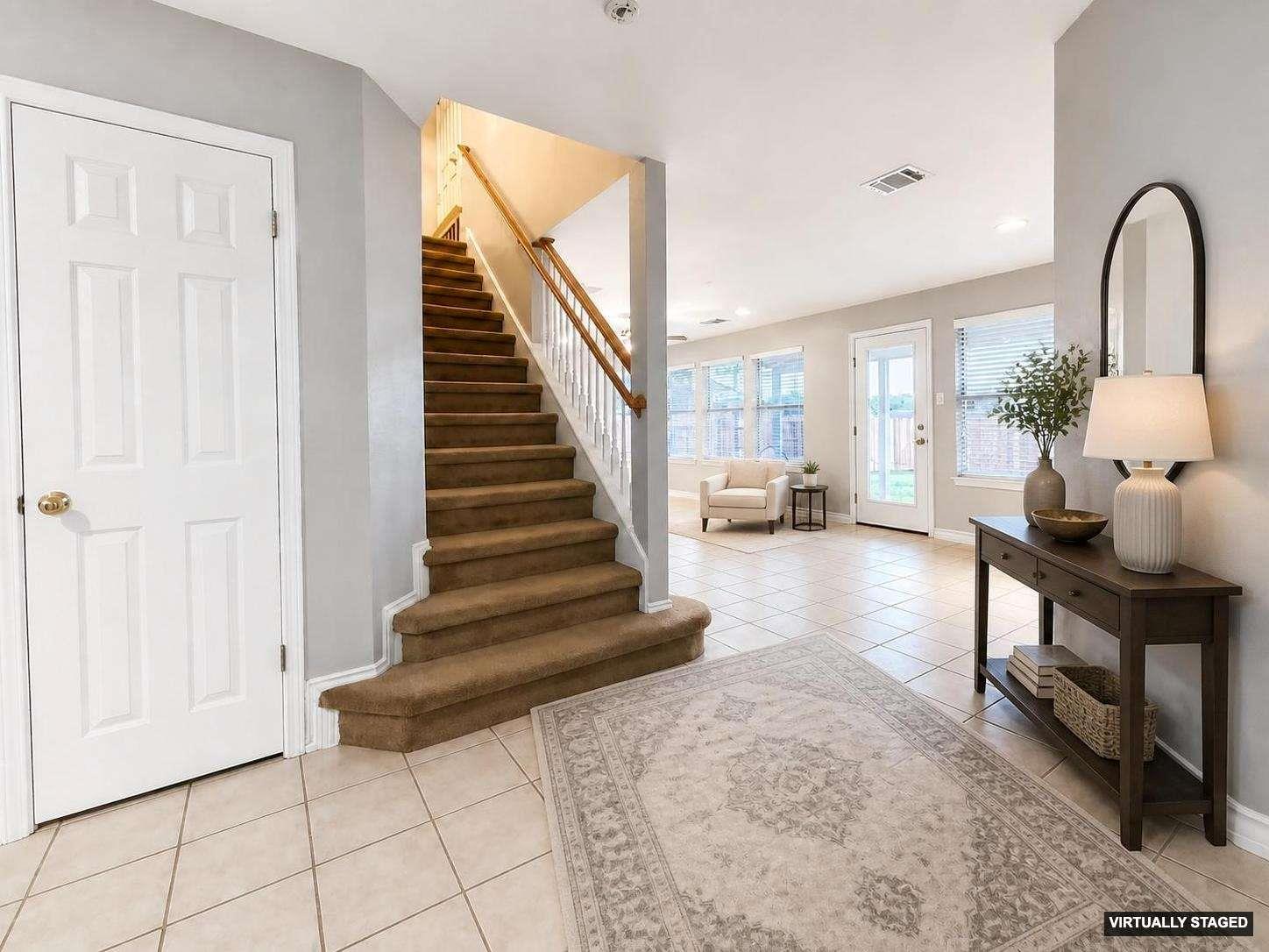 Inviting entryway featuring tile flooring and a carpeted staircase with wood handrails