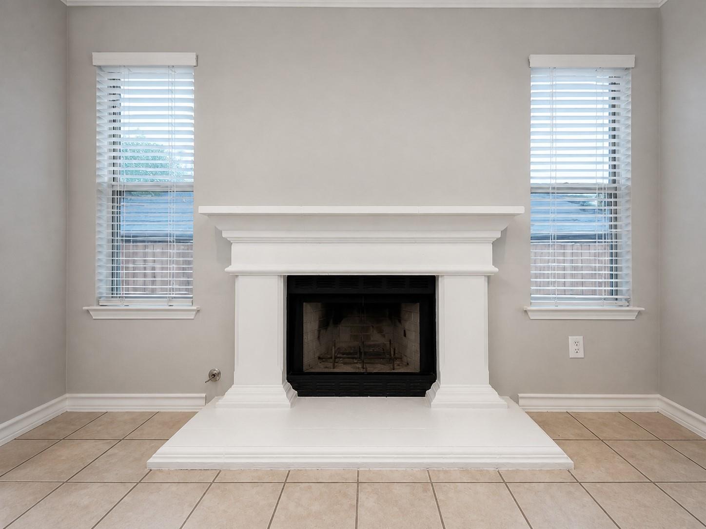 Fireplace with a white mantel and hearth, flanked by two windows with blinds