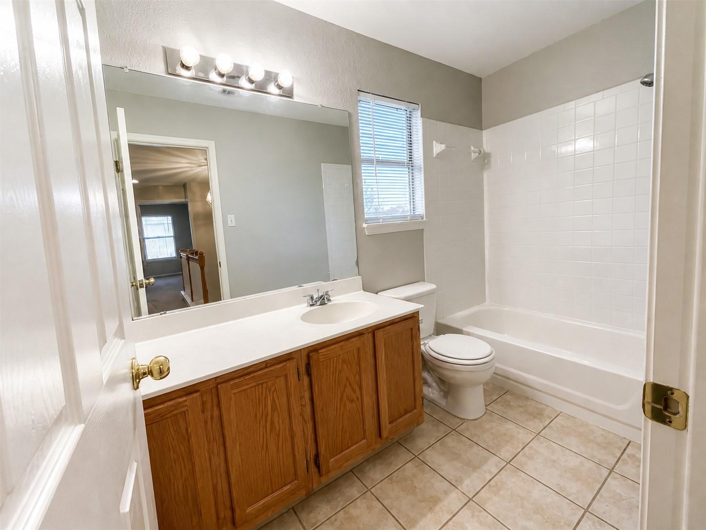 Bathroom featuring a wood-finish vanity with an integrated sink, a white countertop, and a vanity mirror with a four-bulb light fixture