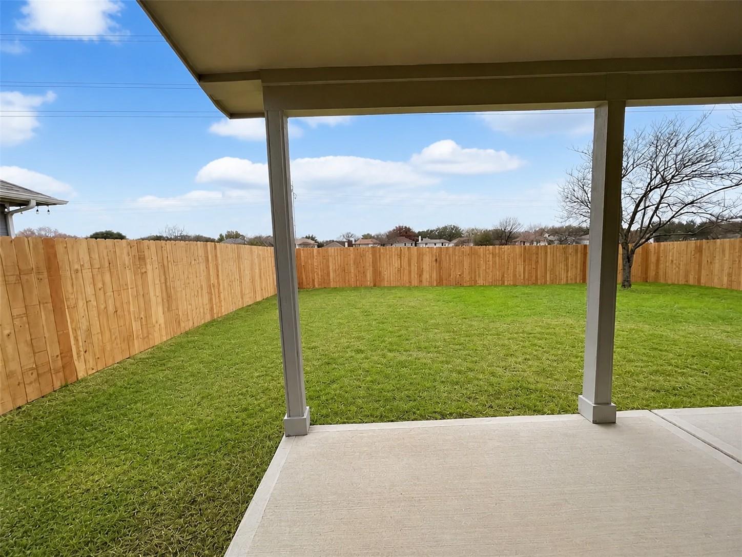 Covered patio with a concrete slab, expansive green lawn, and a perimeter wood fence
