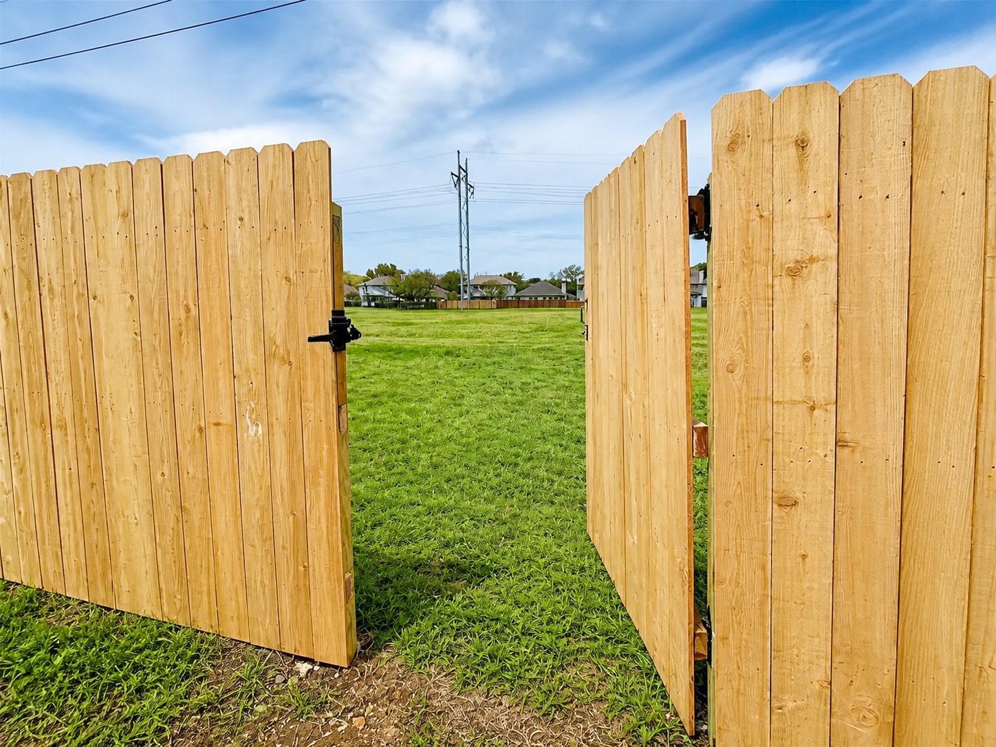 Wooden privacy fence with a black metal latch, opening to a grass area
