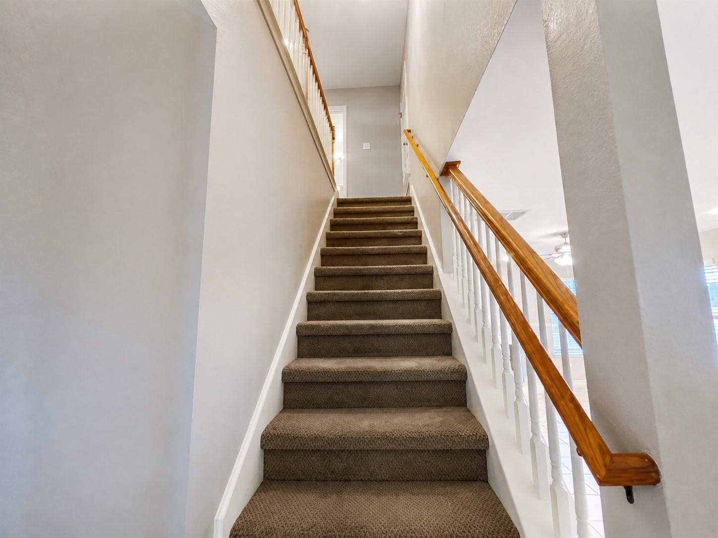 Staircase featuring brown carpeted treads, white risers, and a banister with white balusters and wood-finish handrails