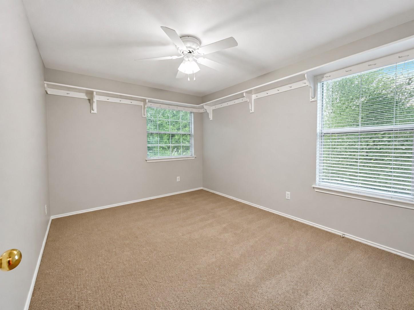 Carpeted interior room featuring two windows with horizontal blinds, a ceiling fan with integrated lighting, and a neutral wall color