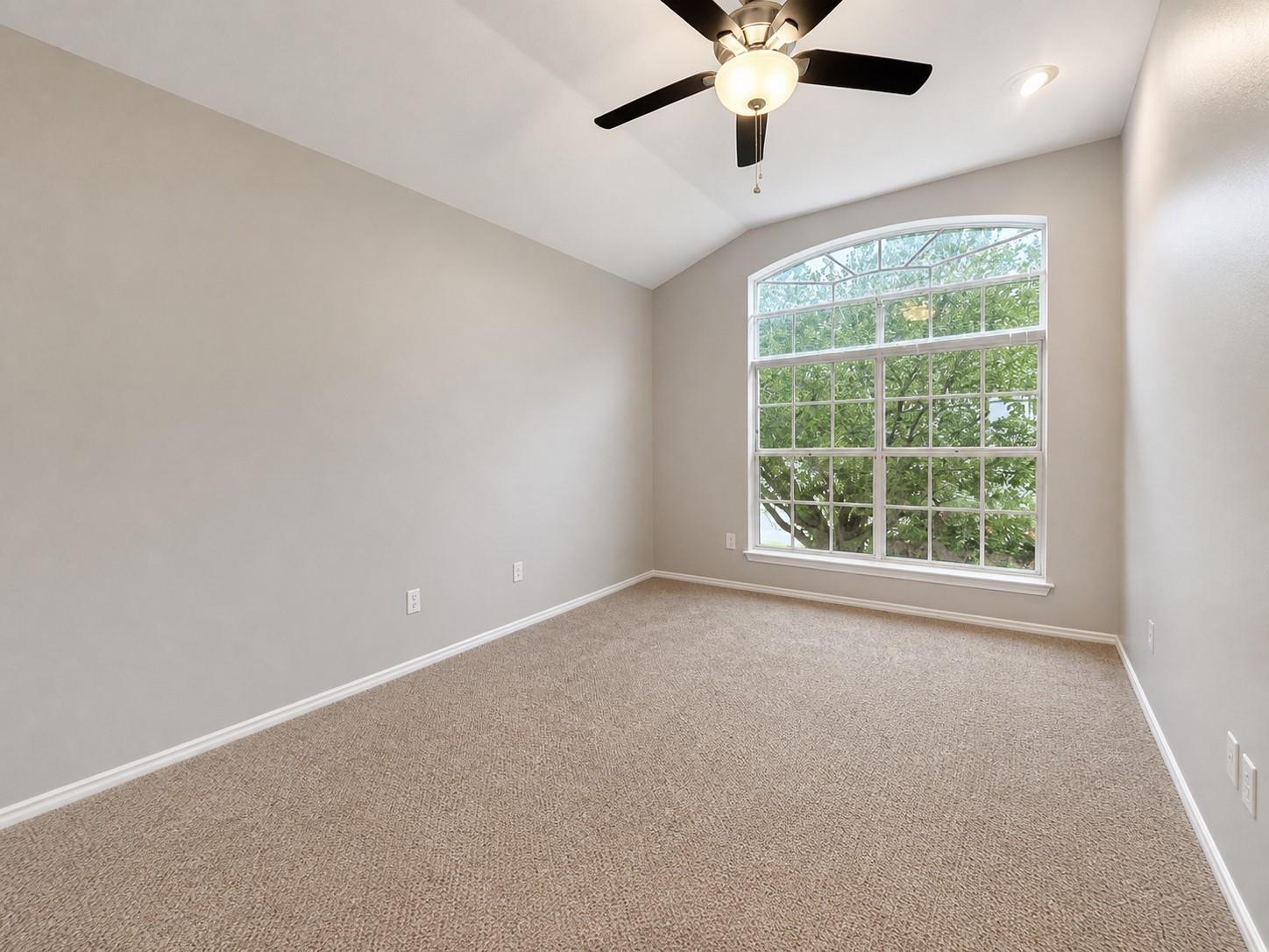 Vaulted ceiling room featuring a large arched window, light beige carpeting, and a ceiling fan with integrated lighting