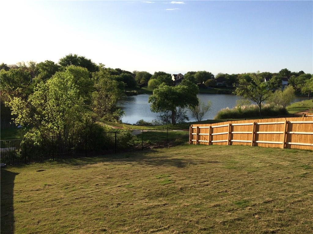 A spacious yard bordered by wood and iron fencing, with tranquil lake views beyond.