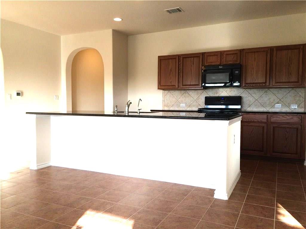 A well-lit kitchen with sleek black countertops, wooden cabinetry, and durable tile flooring awaits your culinary creations.