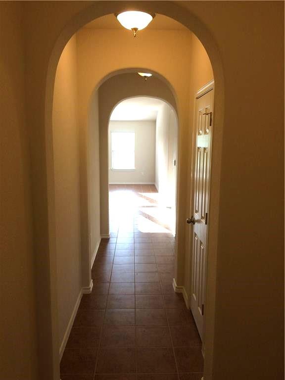 Archways gracefully lead down a well-lit hallway with durable tile flooring.