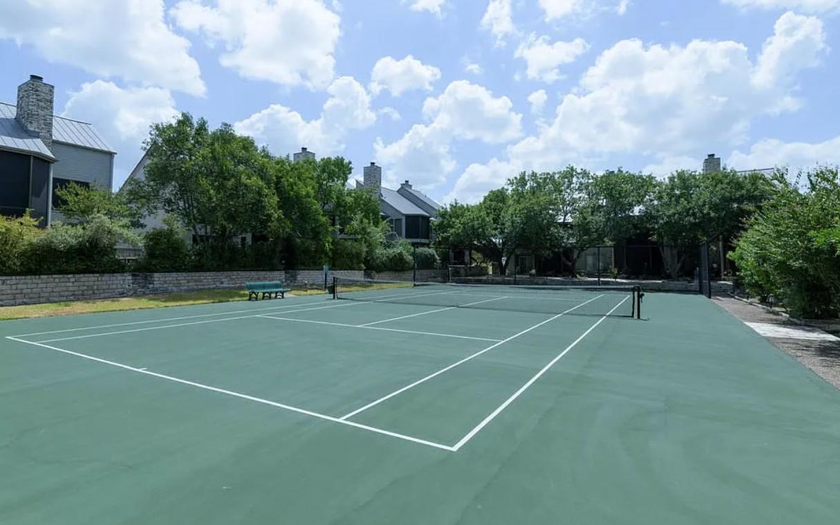 A private tennis court awaits, surrounded by mature trees and charming stone-accented structures.