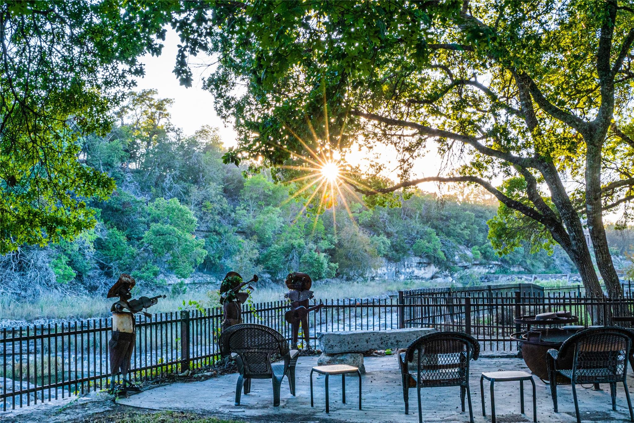 An inviting outdoor patio offers stunning views of the lush, tree-lined landscape and a radiant sunset.
