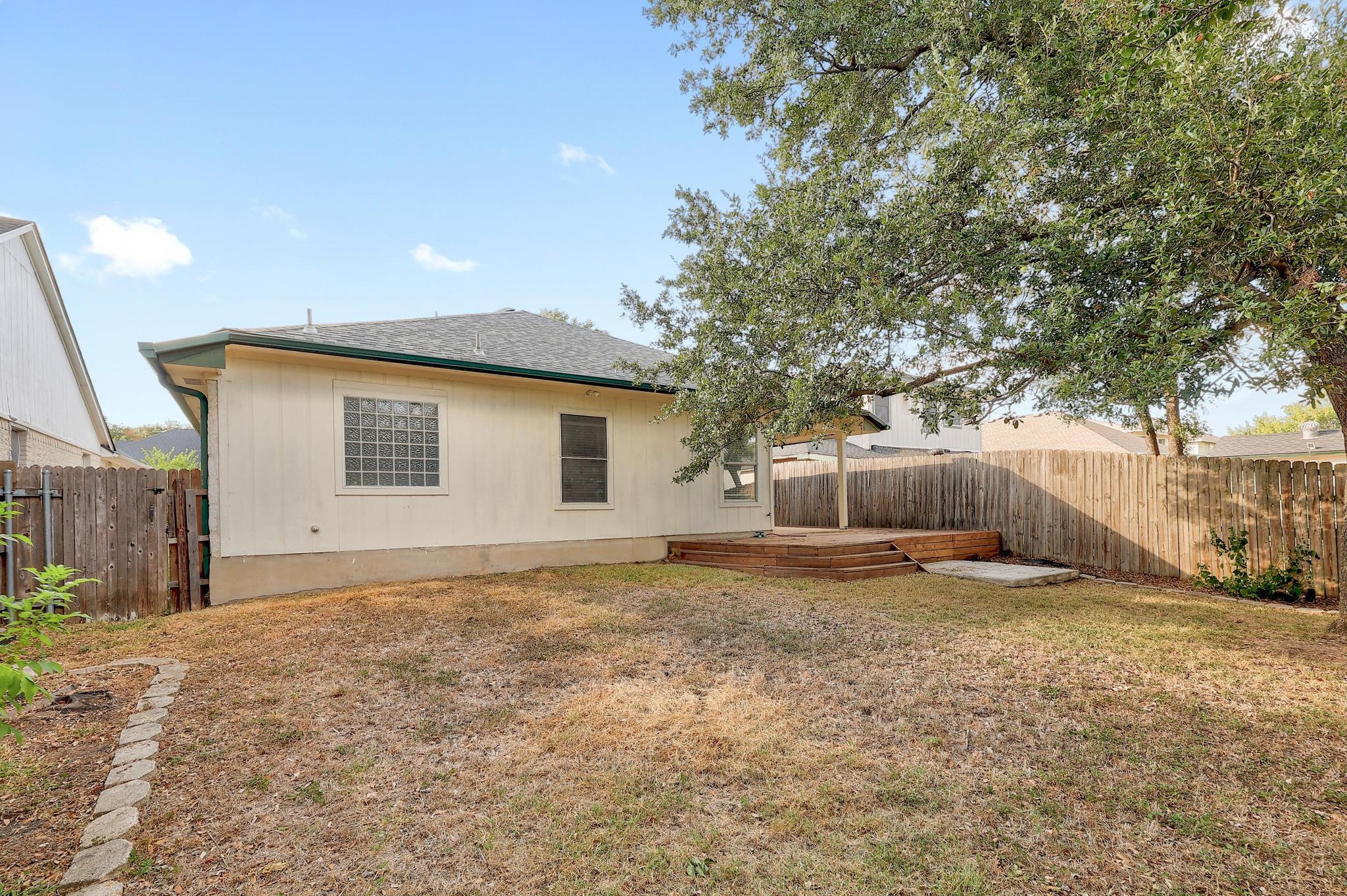 Mature shade trees and a wooden privacy fence frame the grassy backyard area.