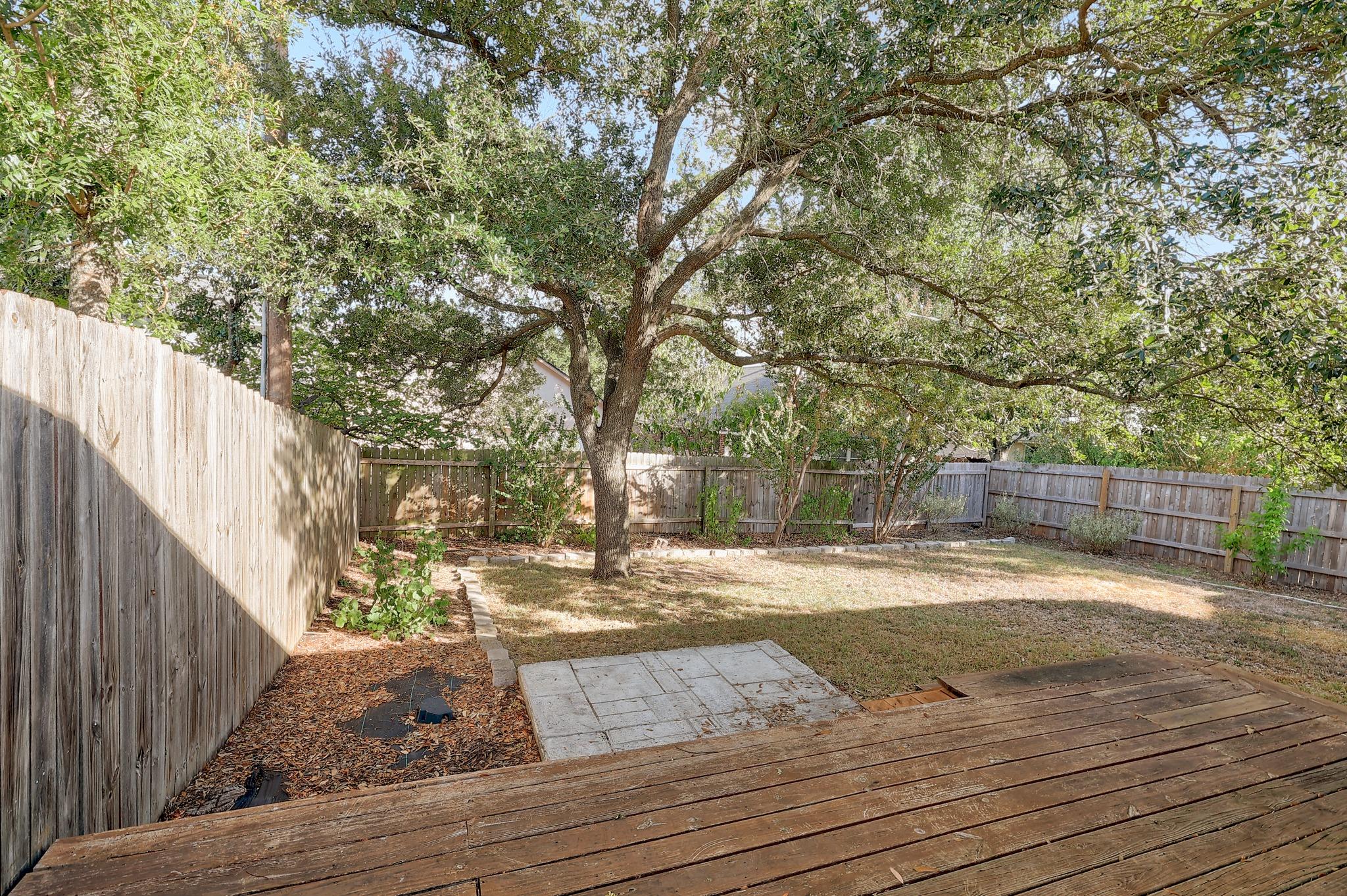 A spacious wooden deck overlooks the fully fenced grassy backyard shaded by mature trees.