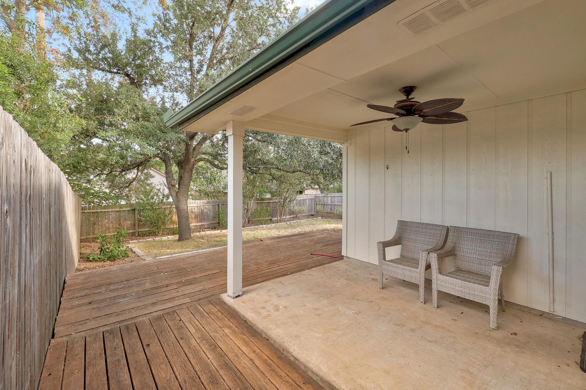 A sheltered back porch transitions smoothly onto an expansive wooden deck surrounded by mature trees.