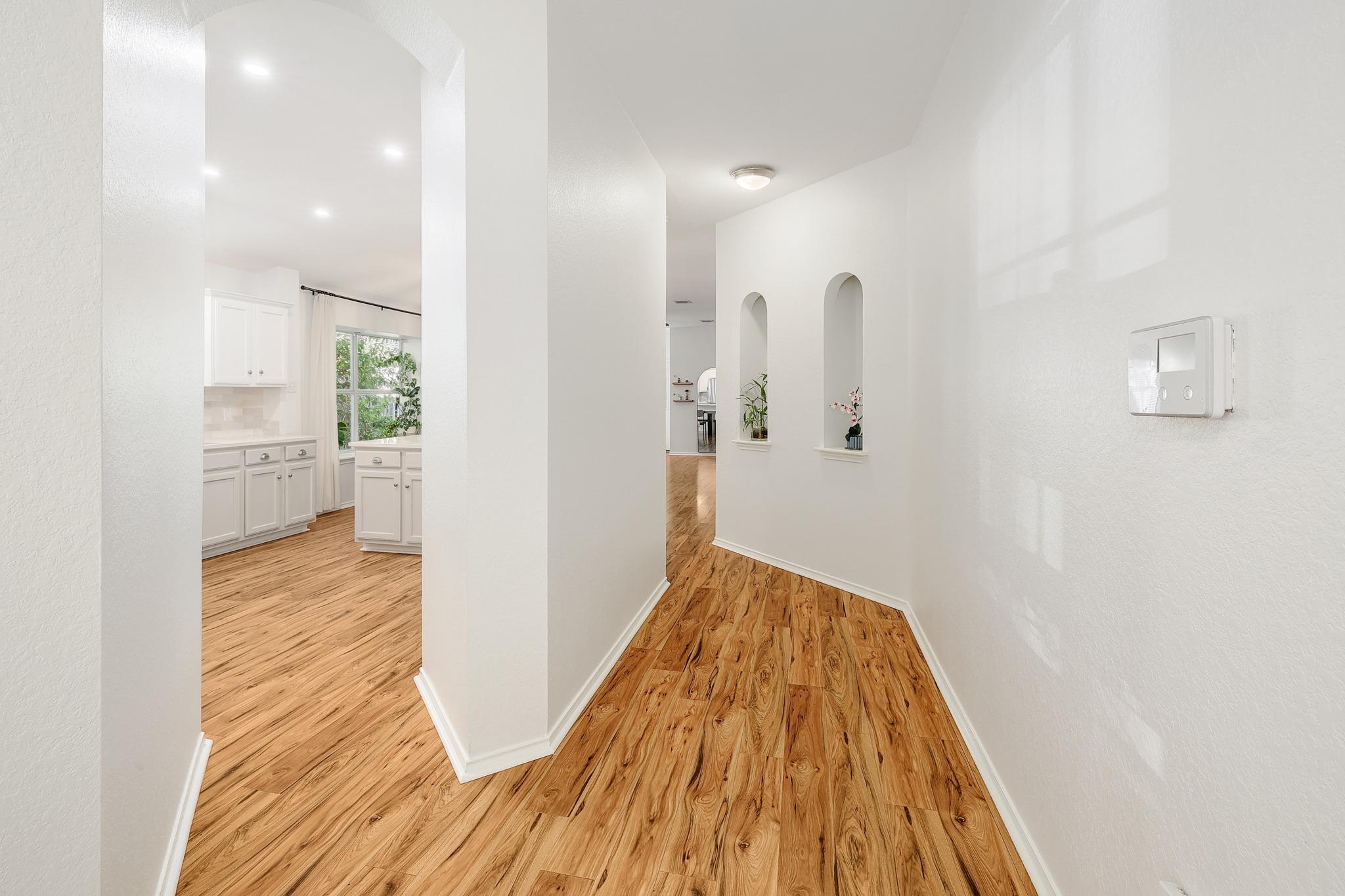 Rich wood-look flooring guides visitors through a bright hallway featuring built-in display niches.
