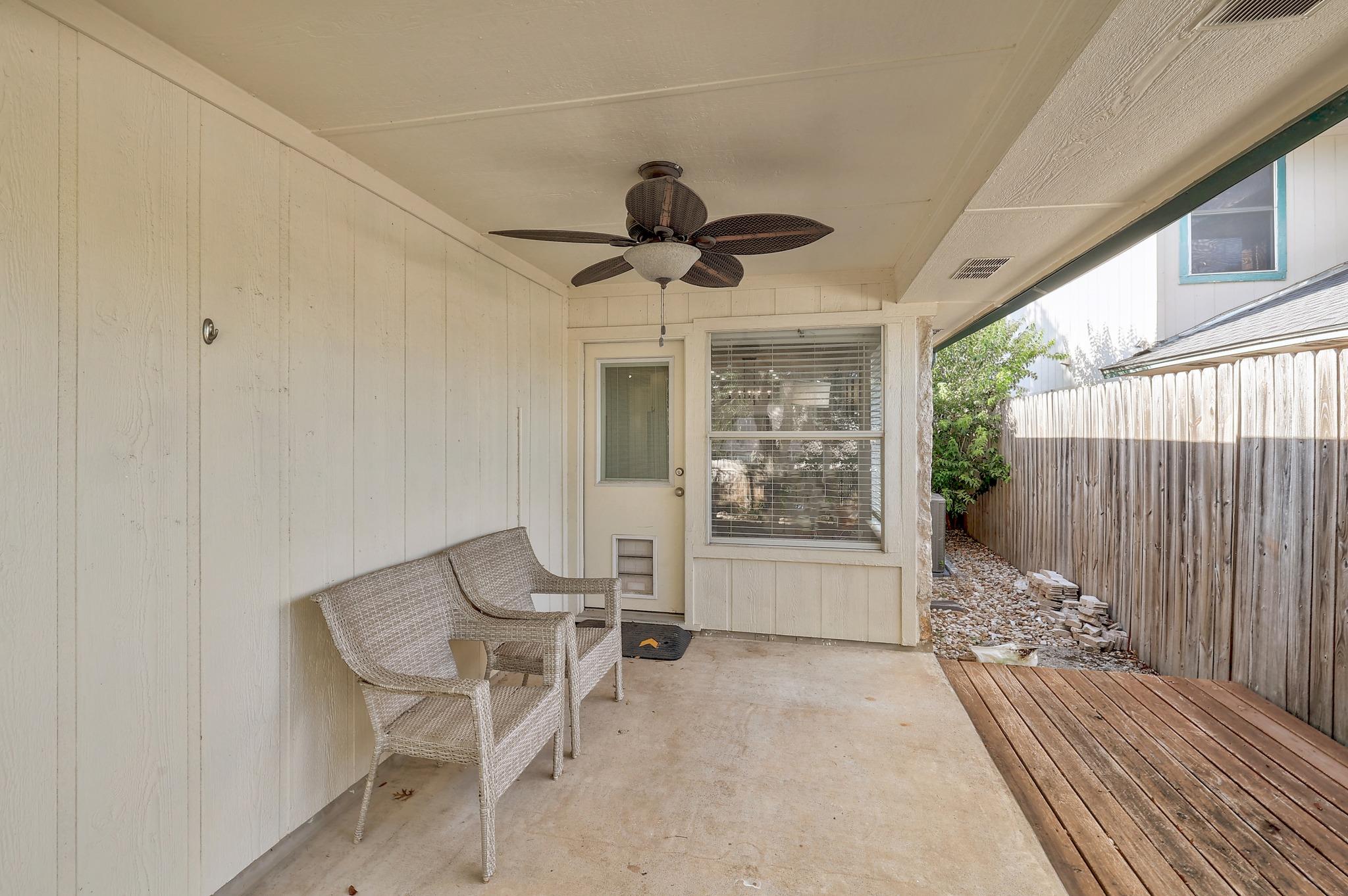 A sheltered back porch transitions smoothly to a wooden deck alongside a tall privacy fence.