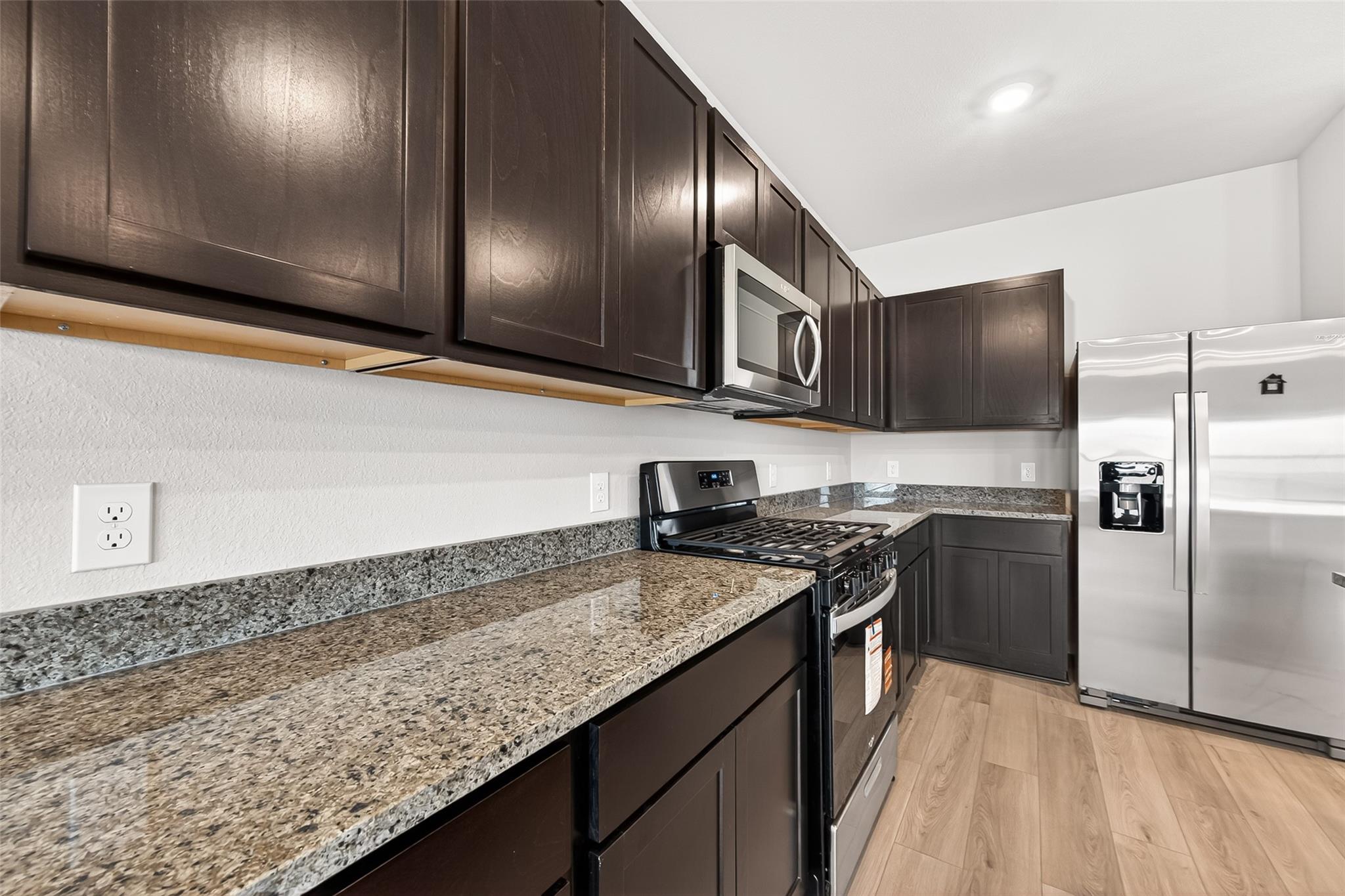 This modern kitchen features sleek dark cabinets, granite countertops, stainless steel appliances, and wood flooring, offering a stylish and functional space.