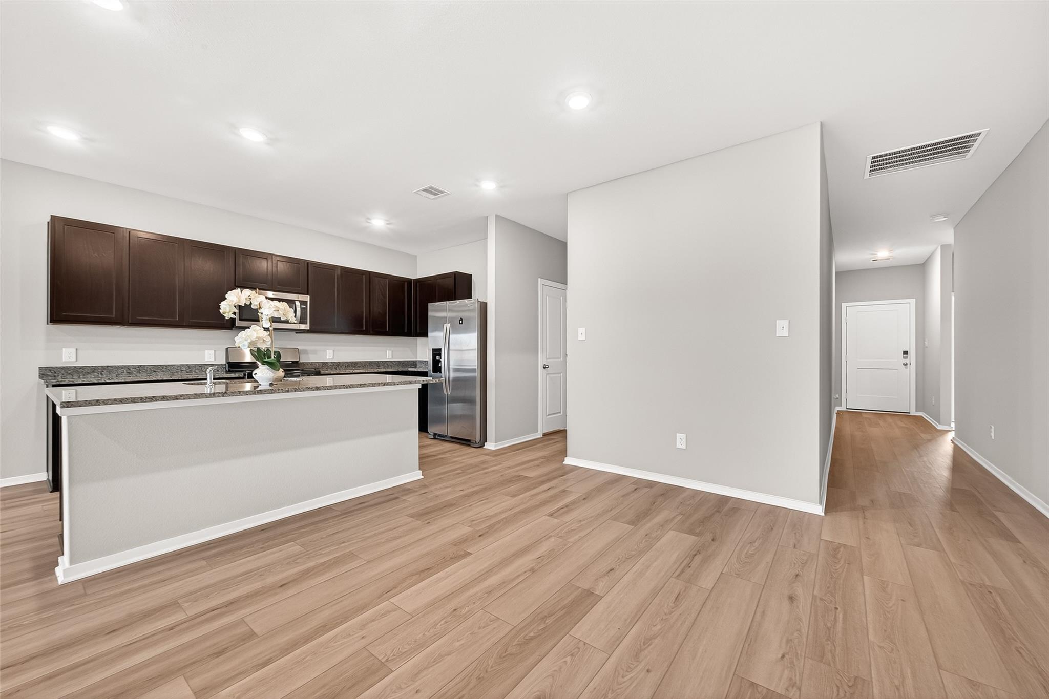 This photo showcases a modern, open-concept kitchen with dark cabinetry, stainless steel appliances, and a spacious island. The light wood flooring and recessed lighting create a bright and inviting atmosphere.
