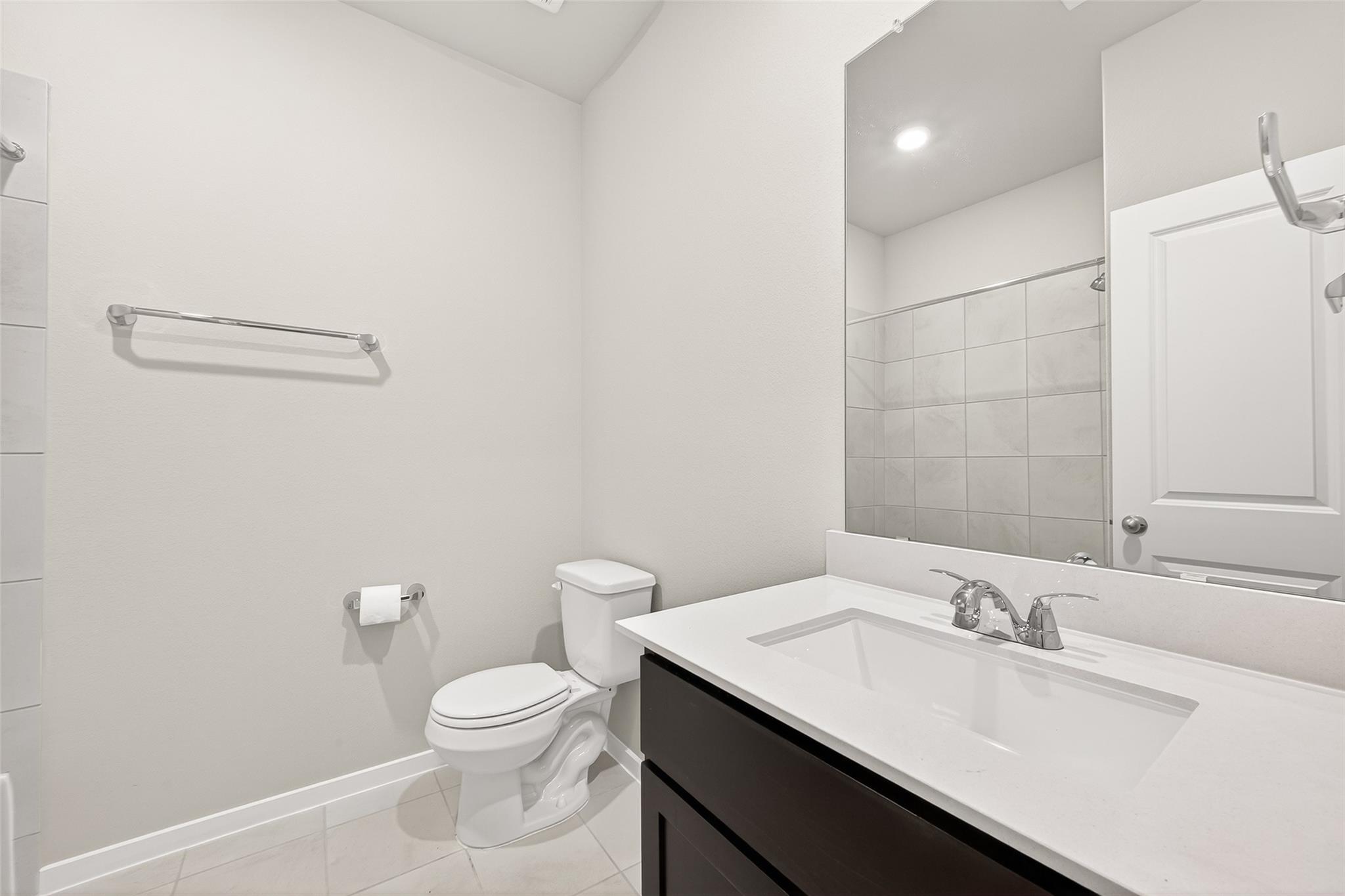 This is a modern bathroom featuring a sleek vanity with a large mirror, a toilet, and a tiled shower area. The space is bright with a clean, minimalist design.