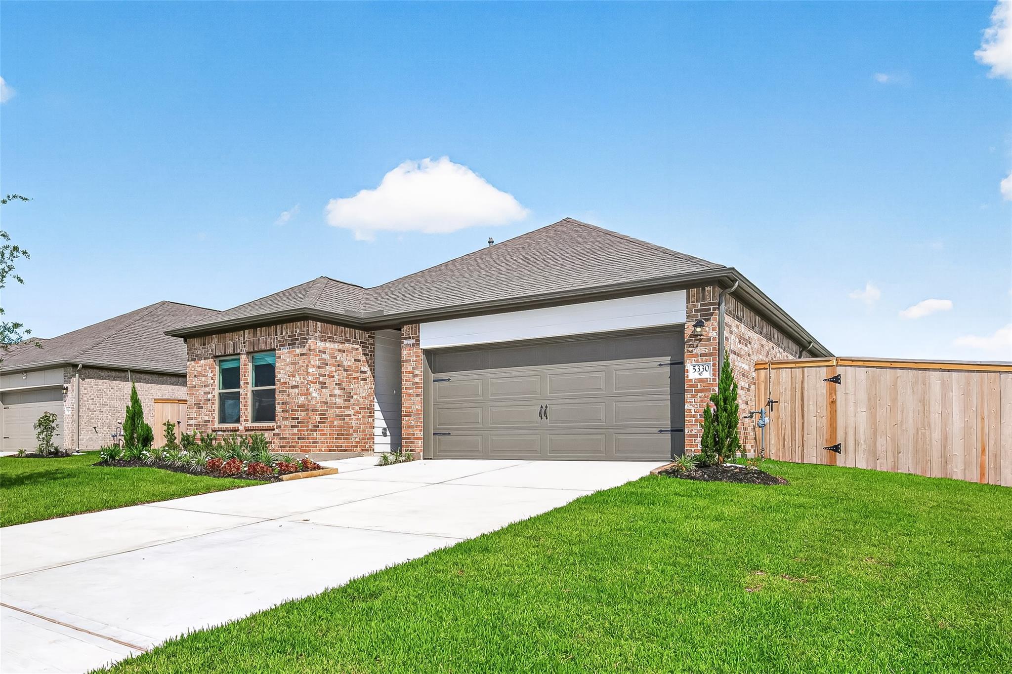 This photo showcases a modern, single-story brick home with a two-car garage. The front yard is well-maintained with fresh landscaping, and the property is bordered by a wooden fence. The driveway is spacious, and the home has a clean, inviting exterior.