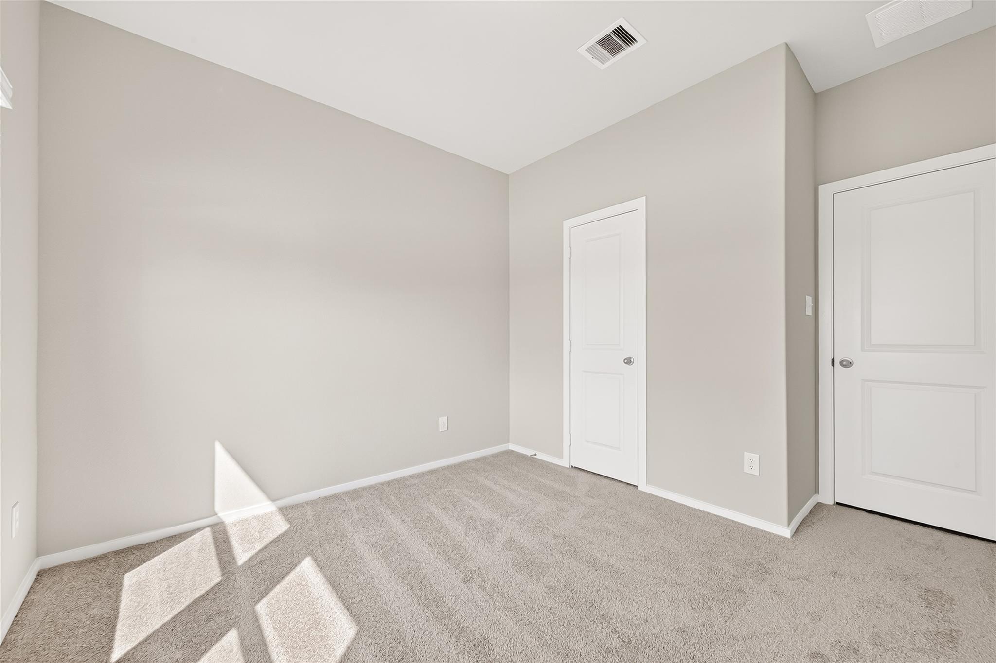 This room features neutral walls, plush carpeting, and two white doors, providing a simple and versatile space with natural light.