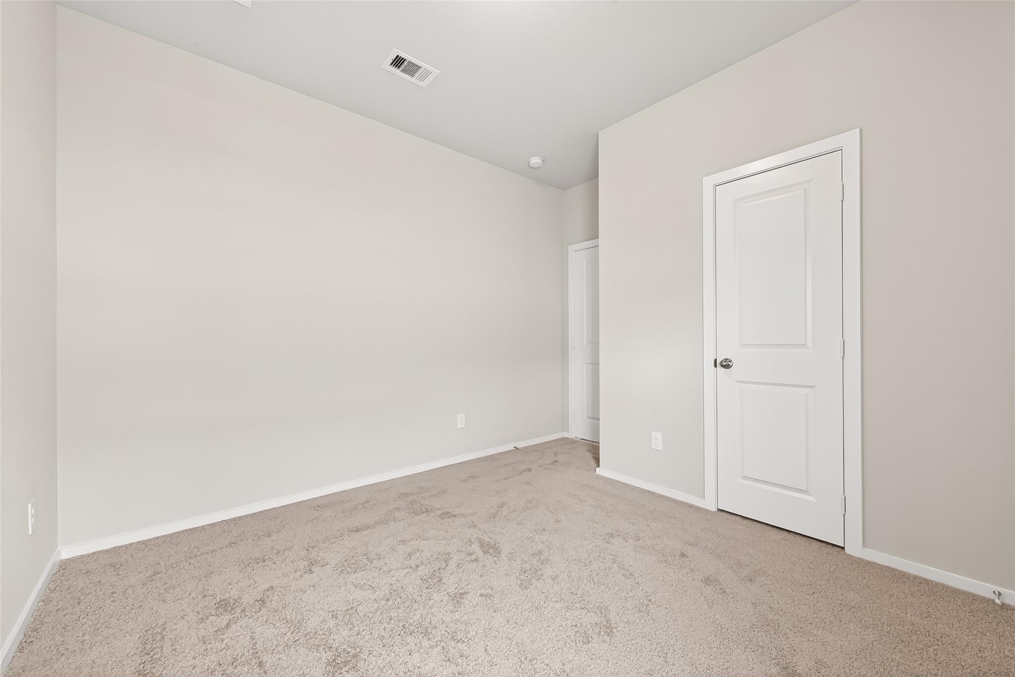 This room features neutral-colored walls and carpet, with two doors and a ceiling vent, offering a clean and simple space ready for personalization.