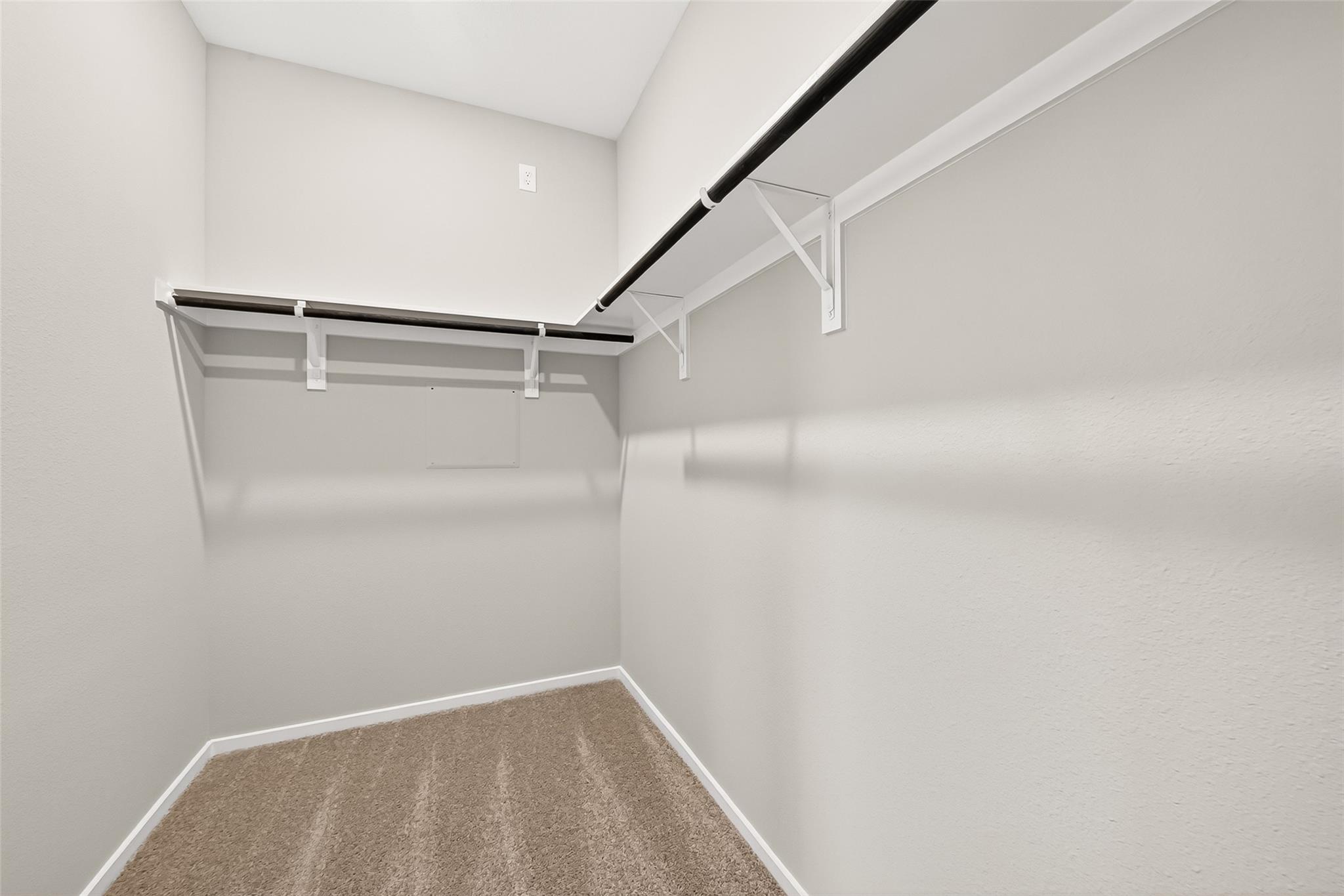 A spacious walk-in closet with neutral walls, carpeted flooring, and a sturdy hanging rod with shelving, ideal for organized storage.