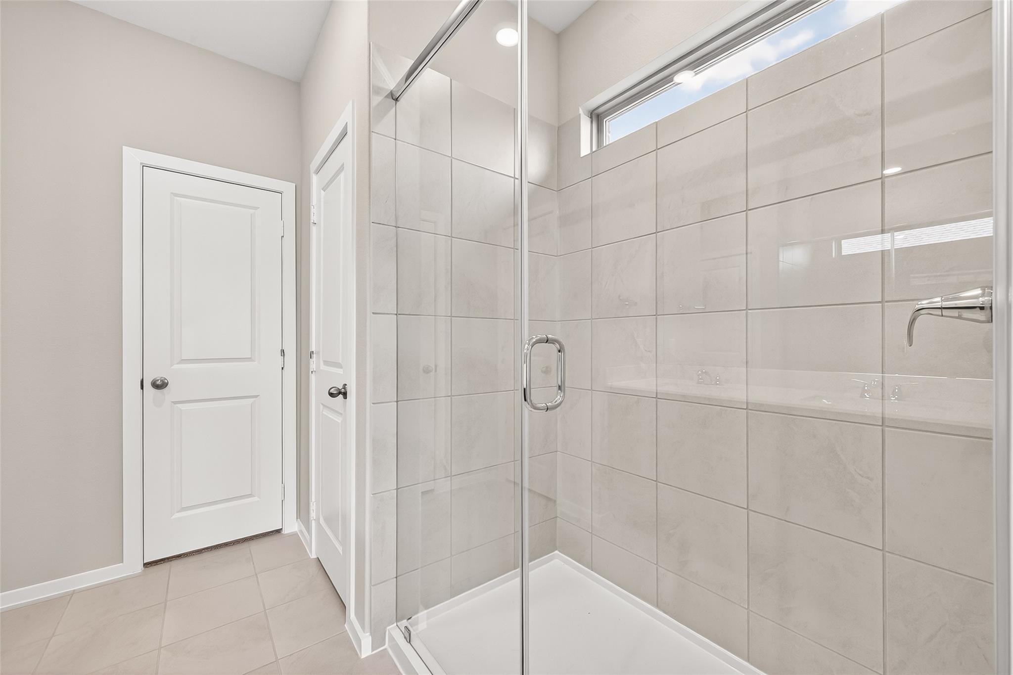 This photo showcases a modern bathroom with a spacious glass-enclosed shower featuring large tiles. The room has a neutral color palette and includes a white door with a sleek handle, offering a clean and contemporary feel.