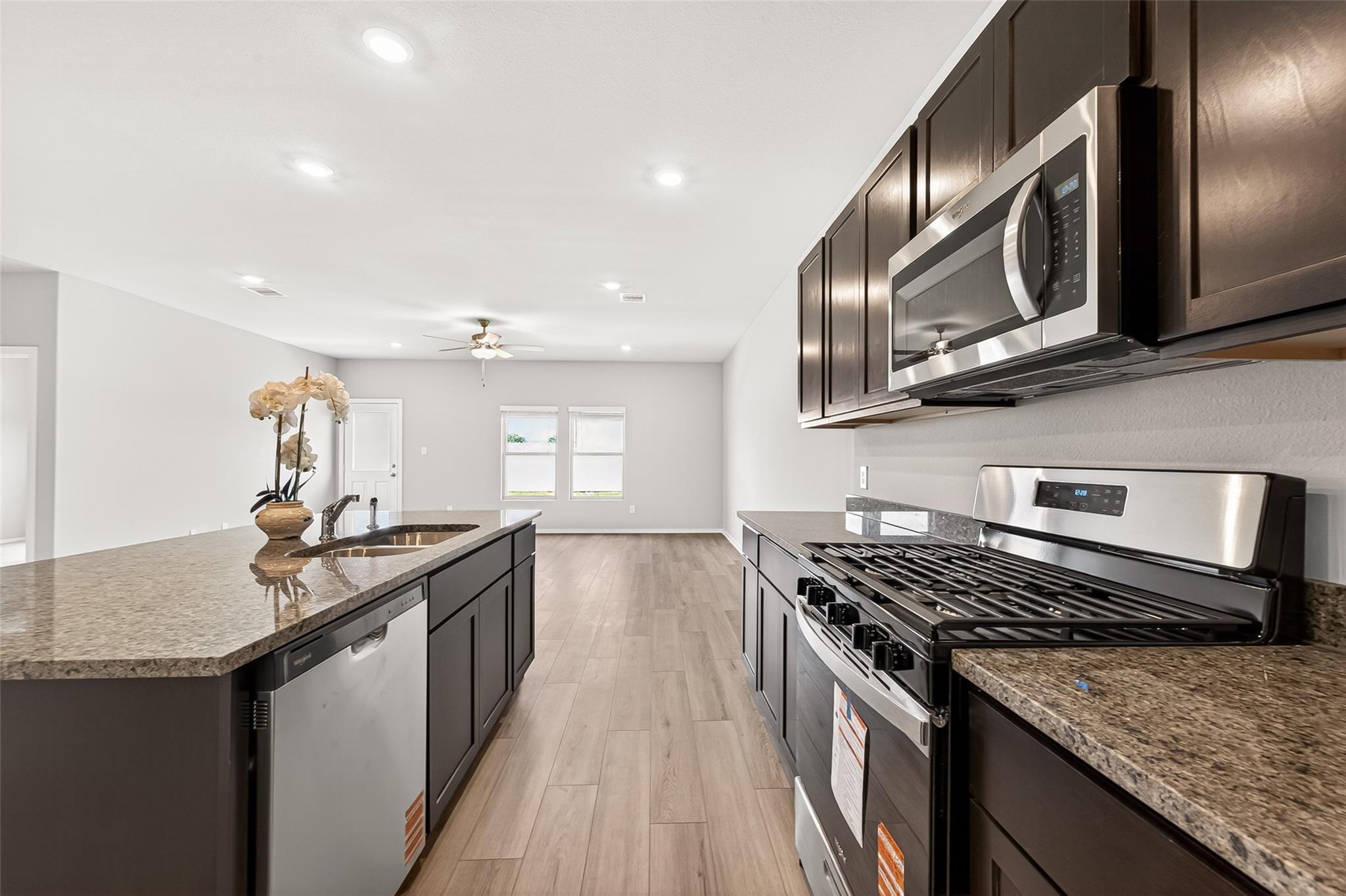 This modern kitchen features sleek dark cabinetry, stainless steel appliances, and a spacious granite countertop with a central island. The open-concept layout flows into a light-filled living area with wood flooring, perfect for entertaining.