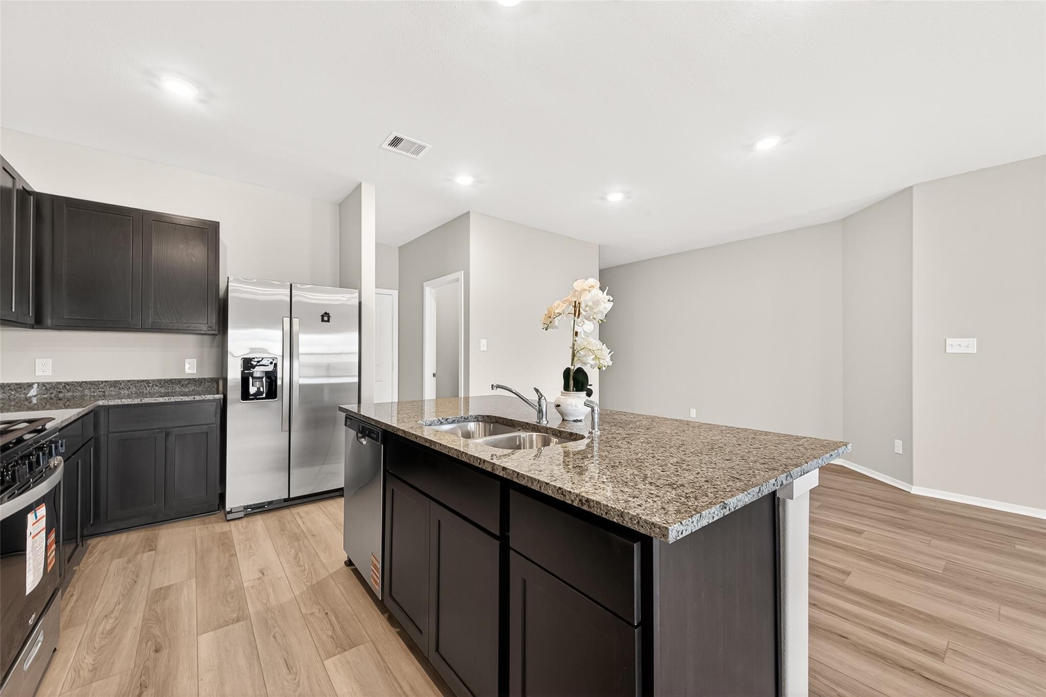 Modern kitchen with sleek dark cabinets, stainless steel appliances, and a spacious granite island. The open layout and light wood flooring create an inviting and functional space.