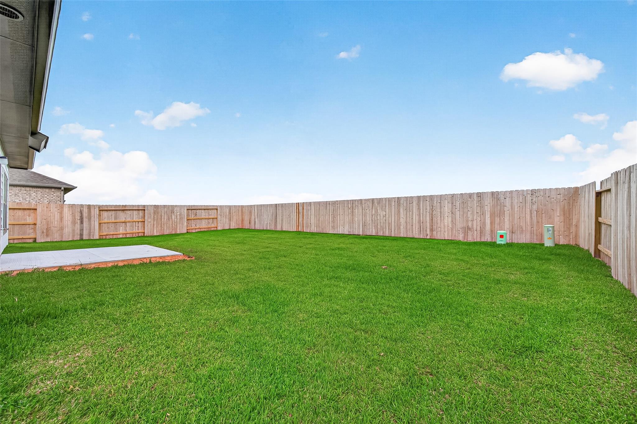 Spacious backyard with lush green grass and a wooden privacy fence, featuring a small concrete patio area ideal for outdoor relaxation or gatherings.