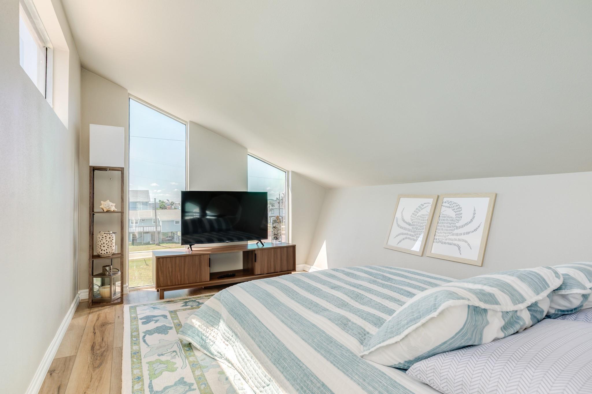 Loft Bedroom – Cozy loft-style sleeping area with sloped ceilings and large windows, offering natural light and a relaxed, private retreat feel.