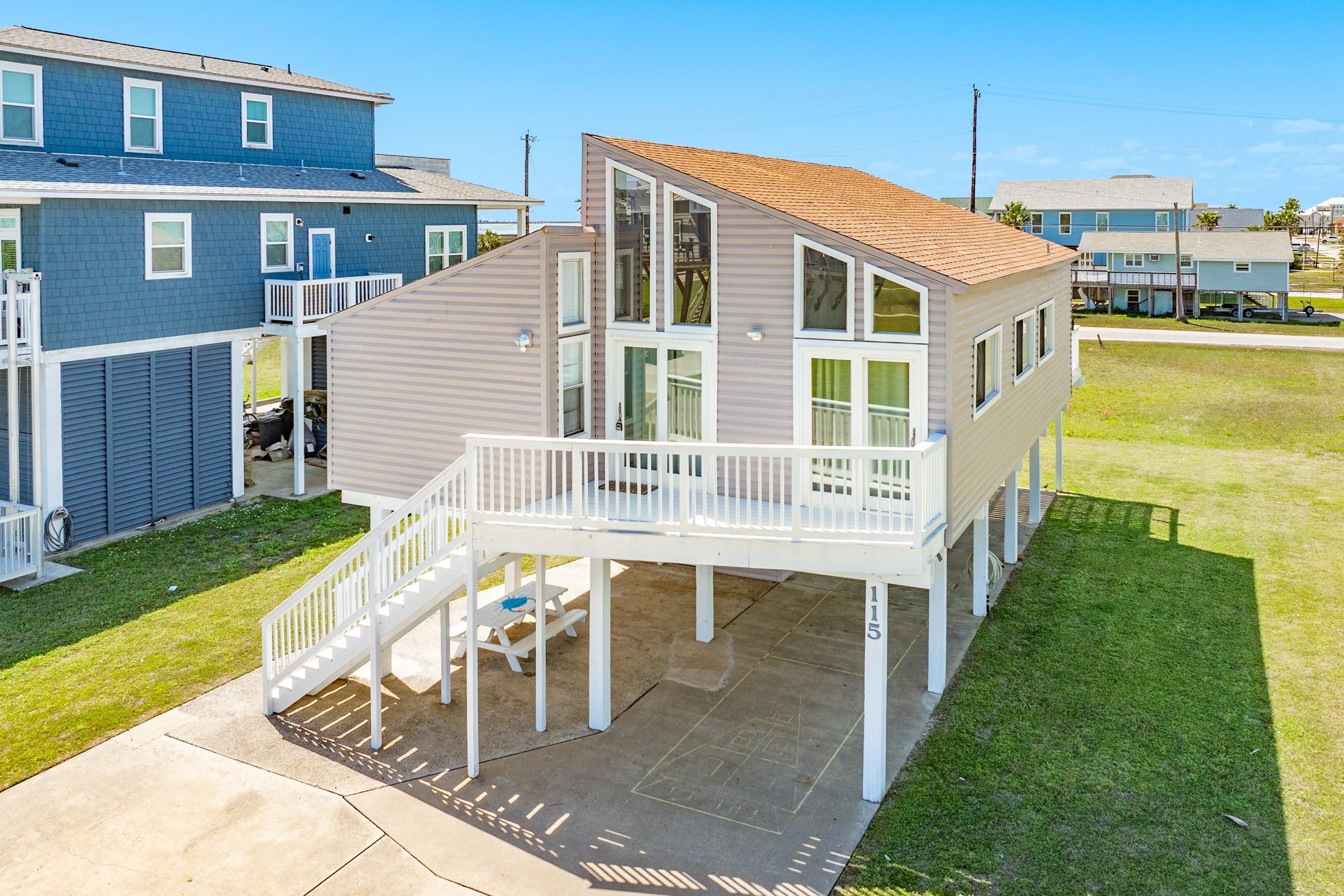 Front Exterior – Elevated coastal home featuring a distinctive sloped roofline and expansive windows that flood the interior with natural light. A spacious upper deck provides the perfect spot for outdoor seating and enjoying the coastal breeze.